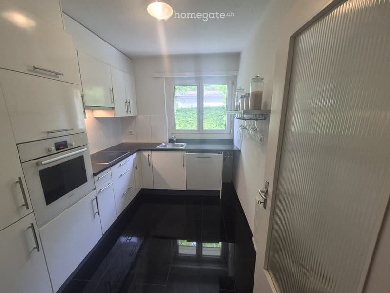 Modern kitchen with white cabinets, black tiled floor, built-in oven, sink, dishwasher, and wine glasses on a shelf.