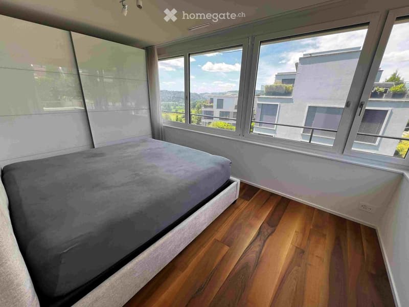 Modern bedroom with wooden flooring, large windows offering a scenic view, and a neatly made bed.