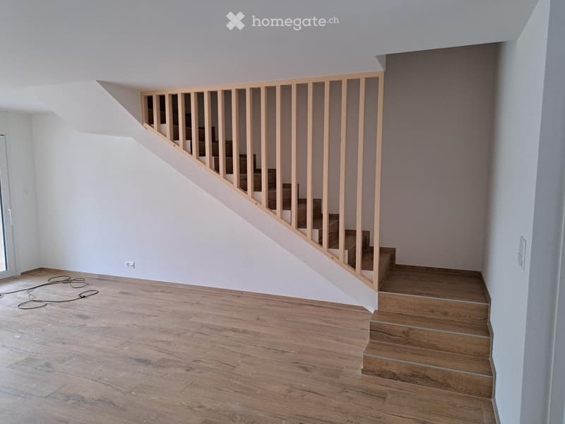 Empty room with wooden flooring and a staircase leading upwards, featuring white walls and a modern wooden railing.