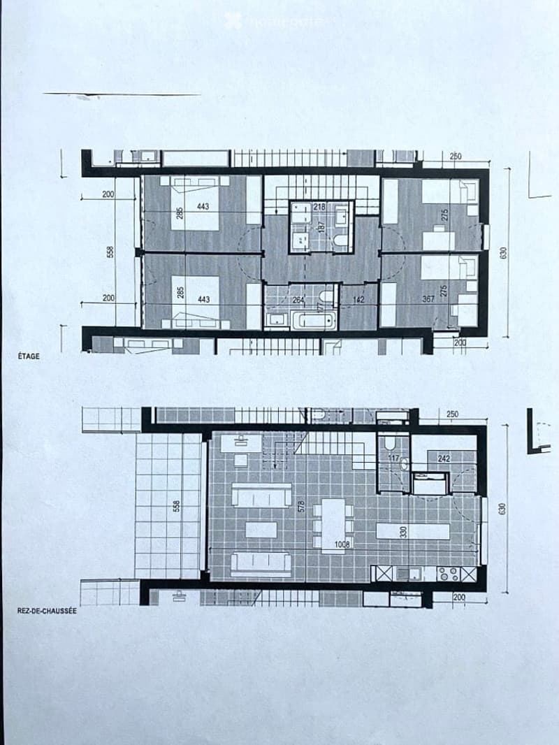 Floor plan of a two-story building with labeled rooms and dimensions. The upper floor includes a large living area, bedrooms, and bathrooms. The ground floor features a kitchen, dining area, and additional rooms.