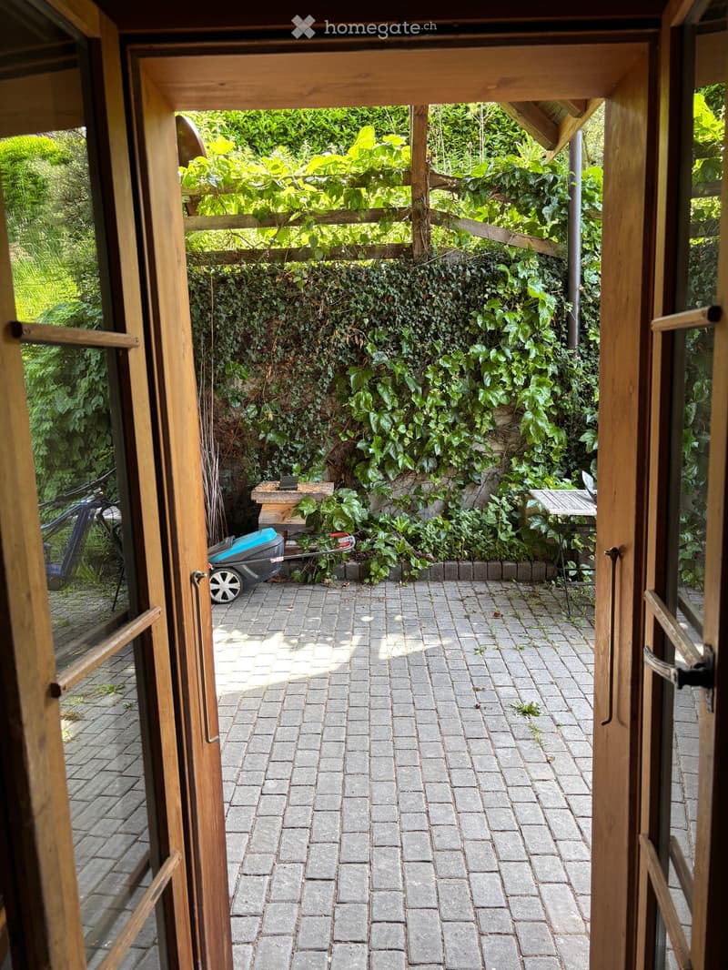 Brick patio with wooden door frame, ivy-covered wall, small table, and lawnmower visible.