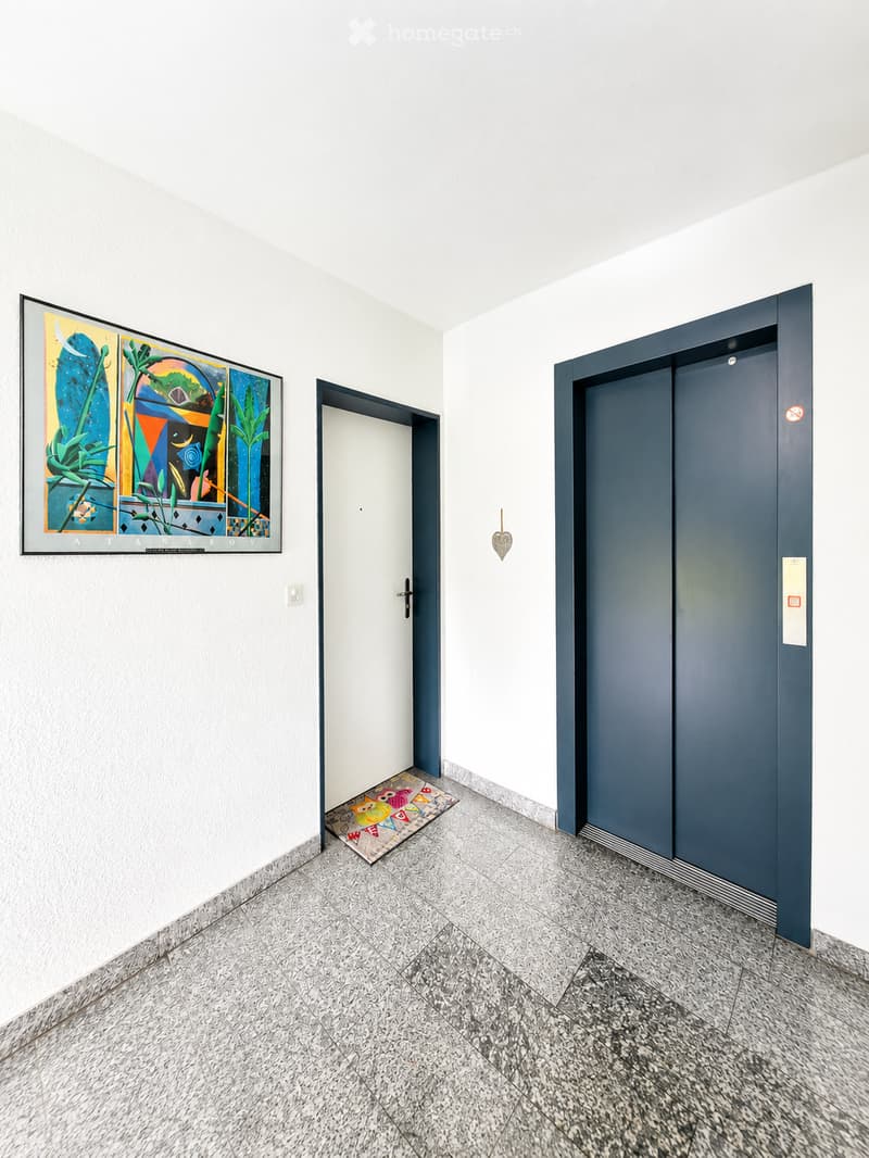 Empty hallway with white walls, marble flooring, a colorful painting, a small rug, and an elevator door.