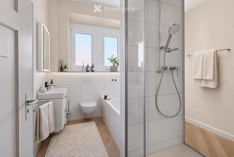 Modern bathroom with white tiles, a glass-enclosed shower, a bathtub, a sink, a toilet, and a window with a small plant on the sill.