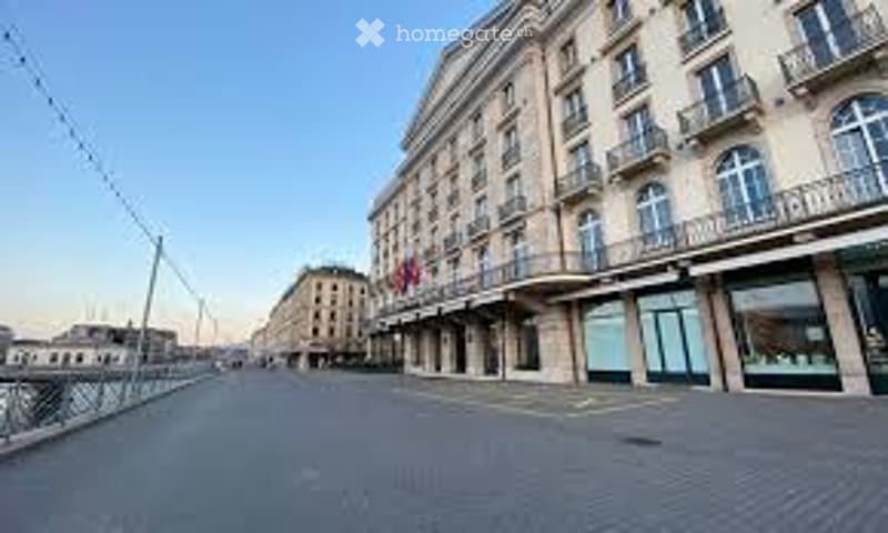 Grand historic building with ornate facade, large windows, and balconies overlooking a waterfront area.