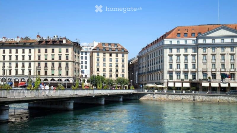 A view of a cityscape with several multi-story buildings, a bridge over a river, and a clear blue sky.