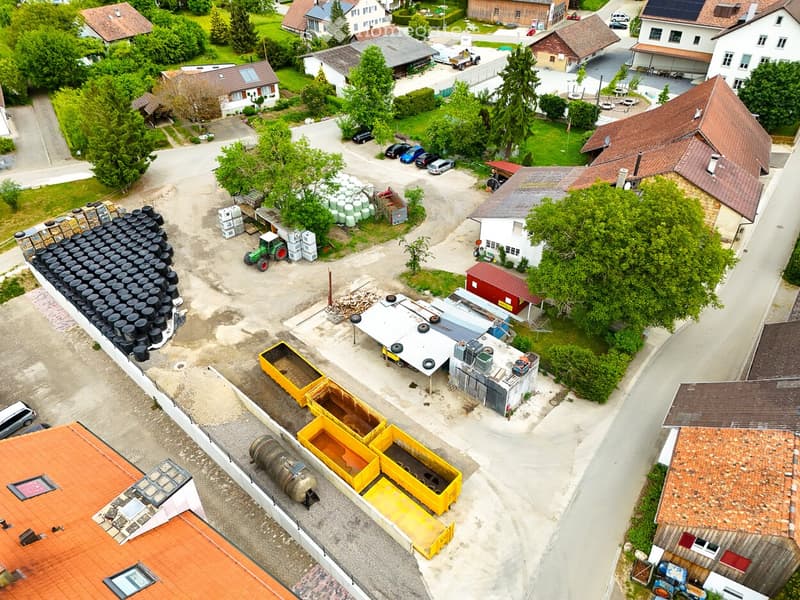 Aerial view of a rural residential area with multiple houses, parking spaces, and scattered vehicles.