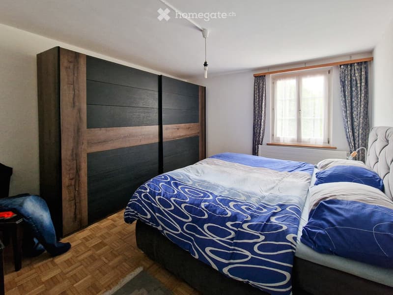 Modern bedroom with a large bed, dark wooden wardrobe, nightstand, and patterned curtains.