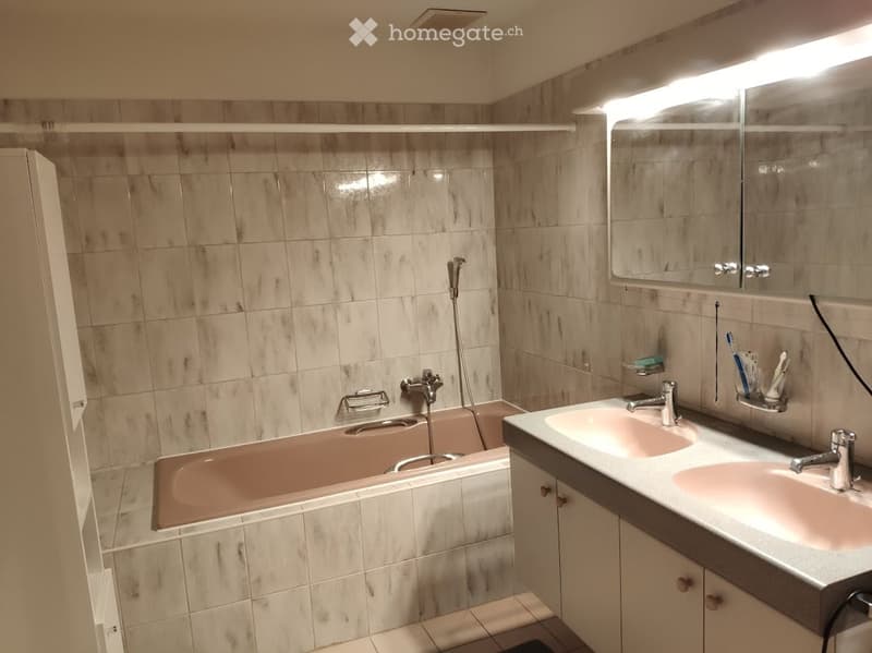 Bathroom with beige tiled walls and floor, a bathtub, a double sink with a mirror above, and a toothbrush holder with toothbrushes.
