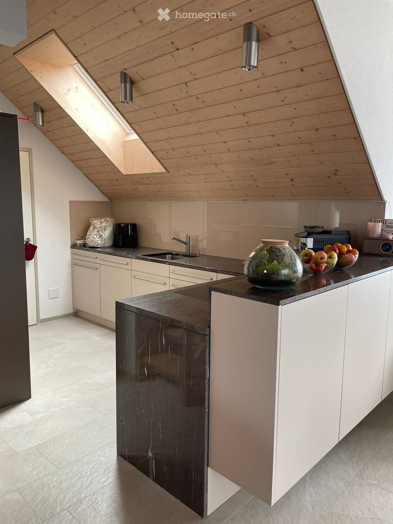 Modern kitchen with white cabinets, dark countertops, and a central island. Features include a sink, faucet, coffee maker, bowl, fruits, vase, and built-in cabinets.