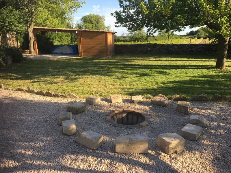 Garden area with a stone fire pit surrounded by large stones, a wooden shed, and a covered seating area.