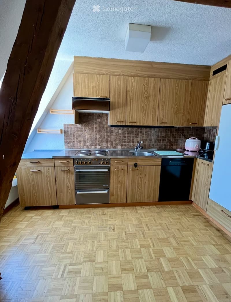 Modern kitchen with wooden cabinets, stainless steel appliances, and herringbone wooden flooring.