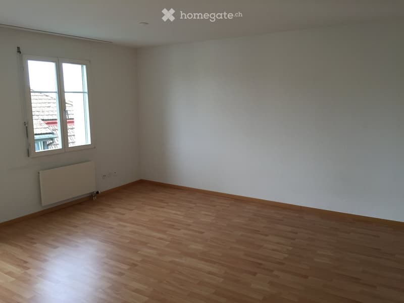 Empty room with wooden flooring, white walls, and a window with a view of a roof.