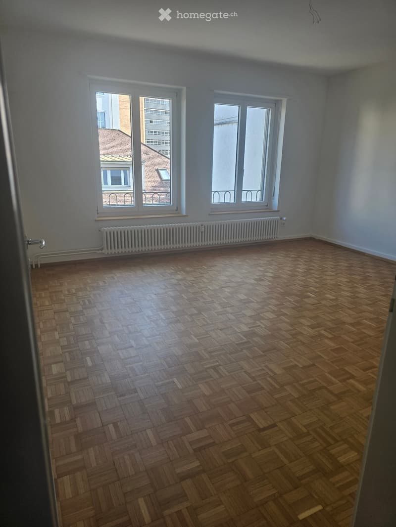 Empty room, hardwood floor, two large windows, two radiators, city view
