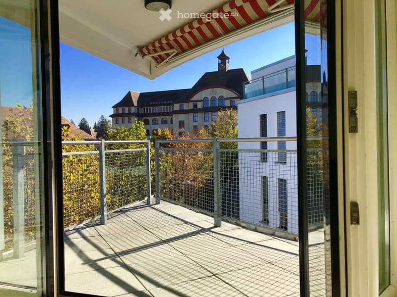 Balcony with metal railing, glass doors, and a view of a historic building with a clock tower and surrounding greenery.
