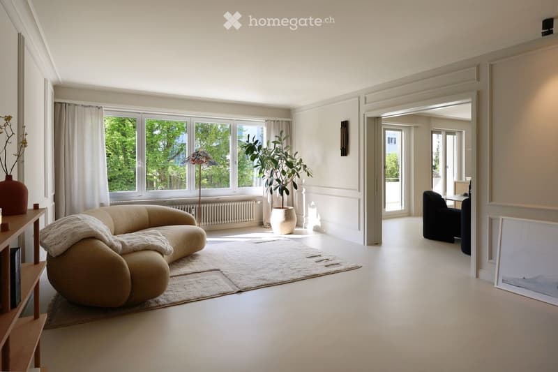 modern living room with white walls, beige sofa, white rug, white curtains, large windows, potted plants, wooden shelf, radiator