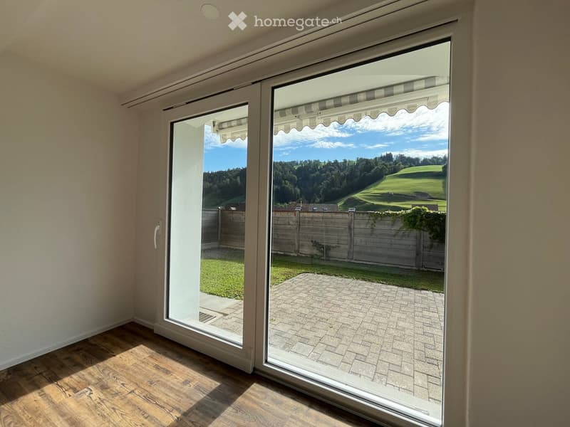 Large sliding glass doors open to a paved patio area with a view of a green landscape and trees.