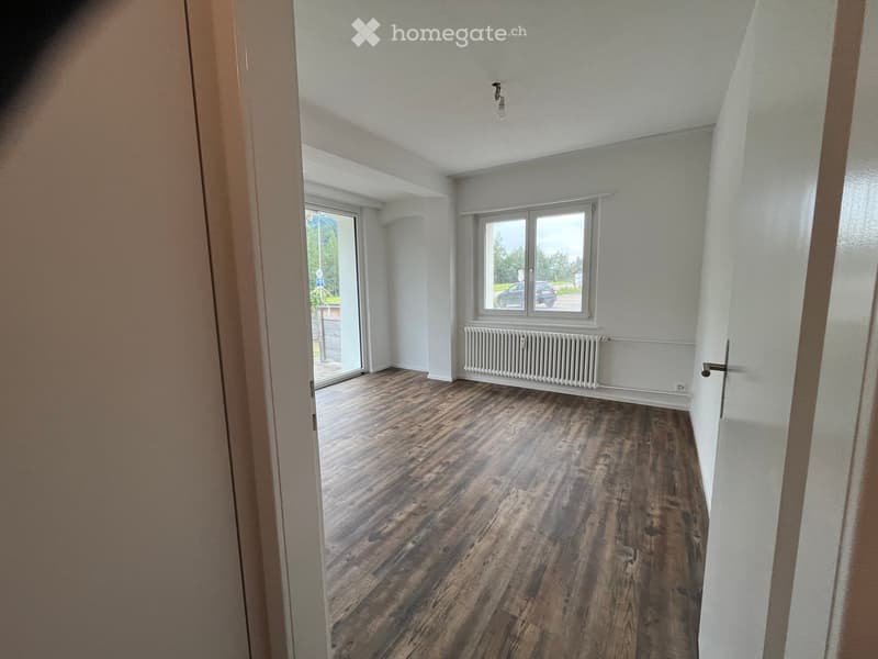 Empty room with wooden flooring, white walls, and large windows offering a view of the outside. No furniture or equipment is present.