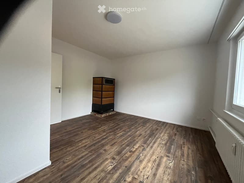 A small, unfurnished room with wooden flooring, white walls, and a single cabinet in the center.