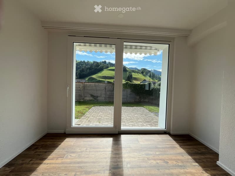 Empty room with wooden flooring, large sliding glass doors opening to a patio and scenic outdoor view.