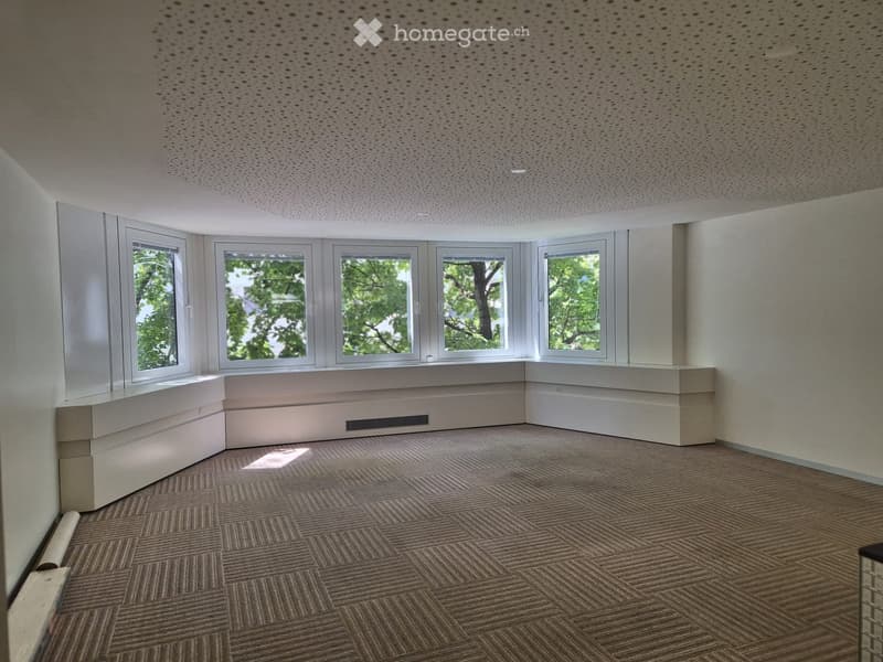 Empty room with carpeted floor, white walls, large windows, and built-in seating along one wall.