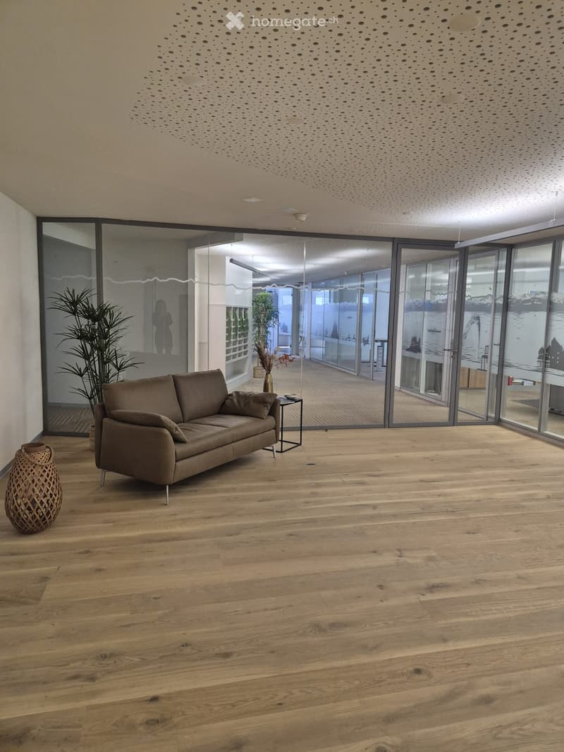 Modern living room with light wooden flooring, large glass sliding doors, a brown sofa, side table, decorative vase, and plants.