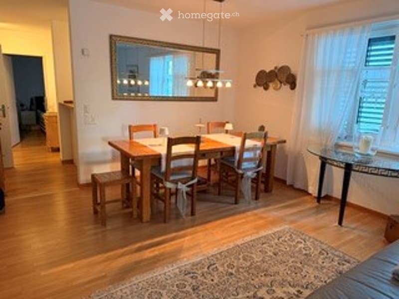 Dining room with wooden floor, dining table, chairs, side table, mirror, and lamp.