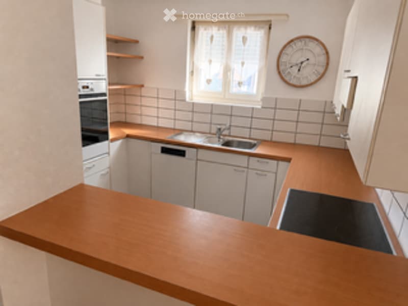 Modern kitchen with white cabinets, wooden countertop, sink, oven, and a clock on the wall.