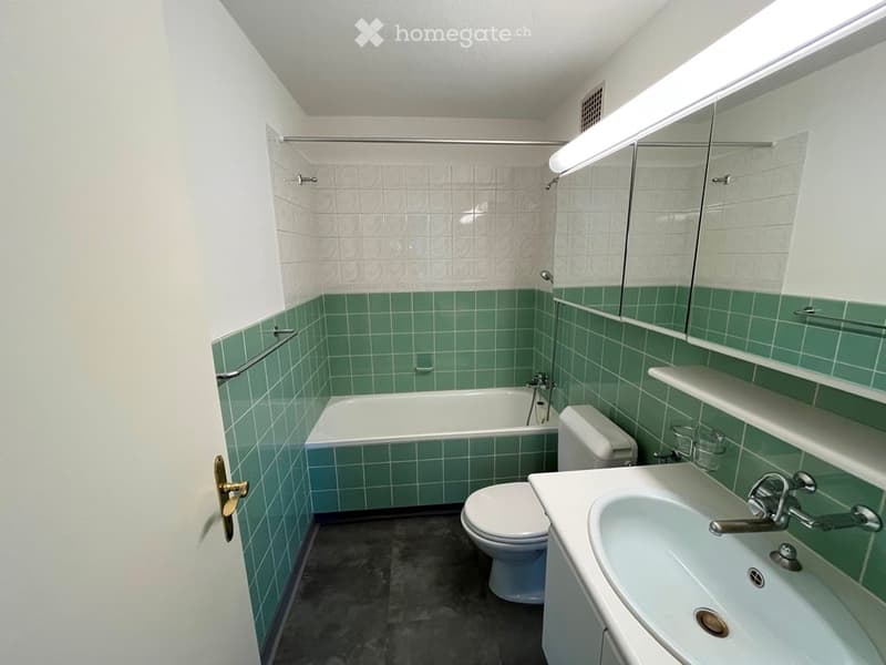 Bathroom with green tiled walls, white fixtures including a bathtub, toilet, sink, and mirrored cabinet.
