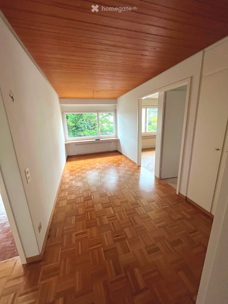 Wooden herringbone-patterned floor and walls, white ceiling, small window at the end, and a mirror on the wall.