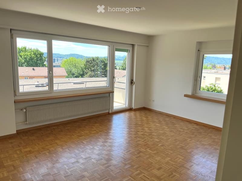 Empty room with wooden flooring, large windows, and a sliding glass door leading to a balcony.