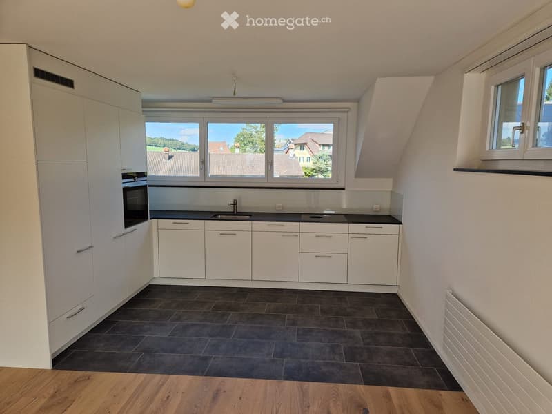 Modern kitchen with white cabinets, dark countertops, and a large window overlooking a residential area.