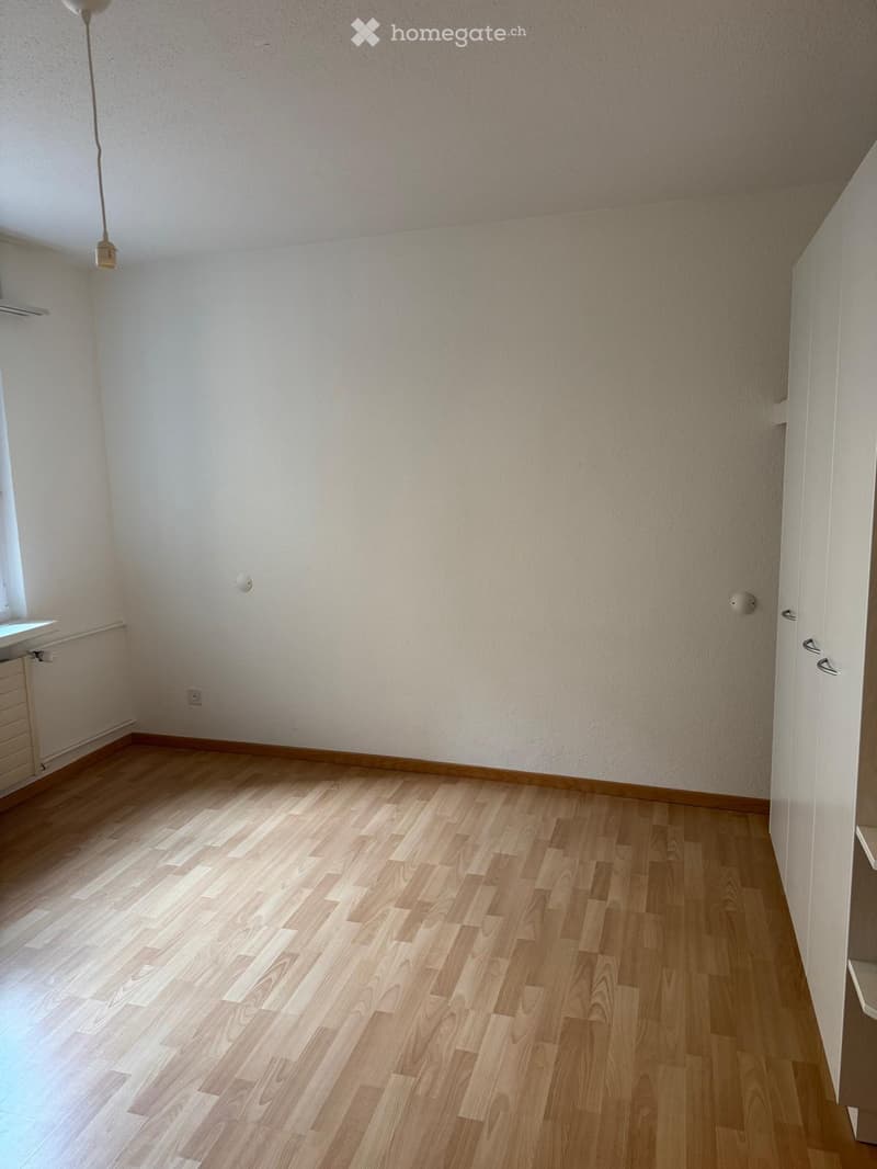 Empty room with light wooden flooring, white walls, and a hanging light fixture. No furniture or equipment is present.
