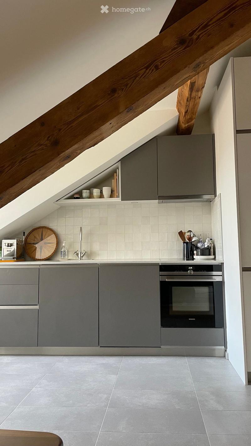 Modern kitchen with grey cabinets, white tiled backsplash, and stainless steel appliances. Features a sink, faucet, oven, and various kitchen utensils on the counter.