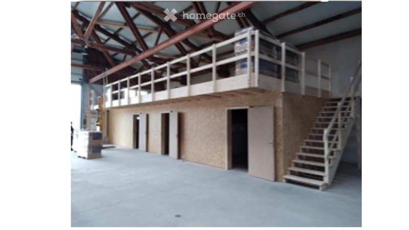 Large industrial-style building with a raised ground floor, metal staircase leading to an upper level, and exposed wooden beams on the ceiling.