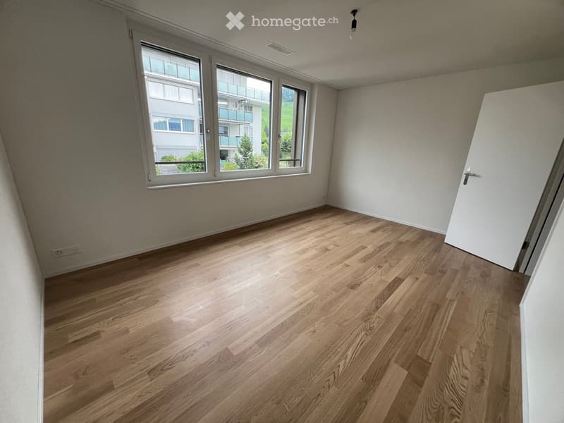 Empty room with light wooden flooring, white walls, large windows, and a door.