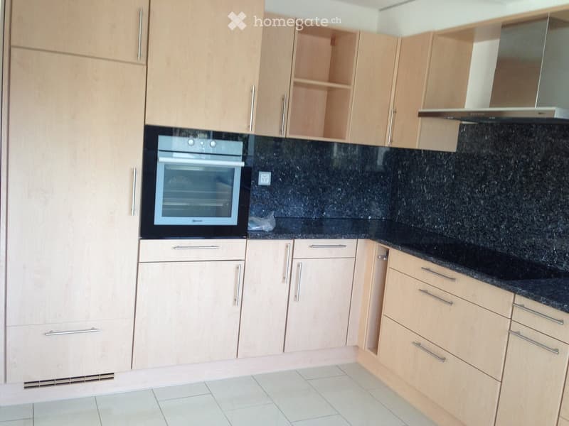 Modern kitchen with light wood cabinets, black granite countertops, and a built-in oven.