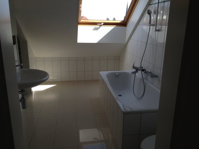 Bright bathroom with a bathtub, sink, and toilet, featuring a skylight window and tiled walls and floor.