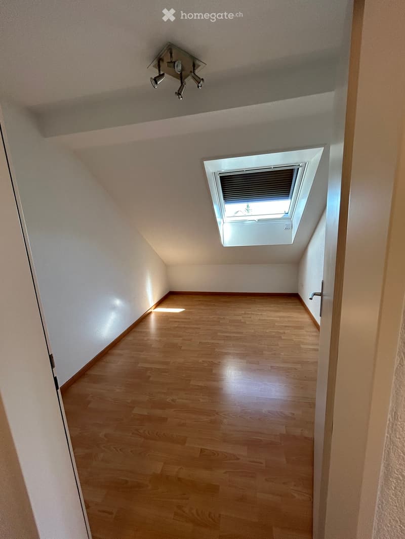 Empty room with wooden flooring, white walls, and a skylight window at the far end.