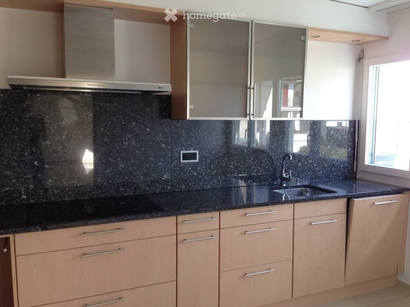Modern kitchen with light wooden cabinets, granite countertops, and stainless steel appliances including a range hood and sink.