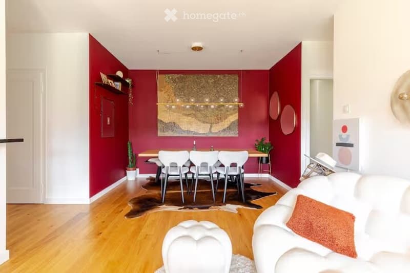 Modern living room with red accent walls, white sofa, dining table with chairs, and decorative elements including a large artwork and plants.