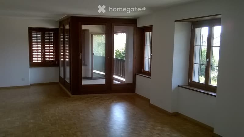 Empty room with wooden flooring, large windows, and sliding glass doors leading to a balcony.