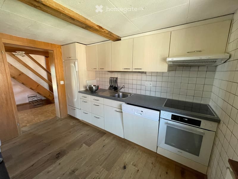 Modern kitchen with white cabinets, wooden flooring, stainless steel appliances including an oven, dishwasher, and sink, with a bowl and utensils on the counter.
