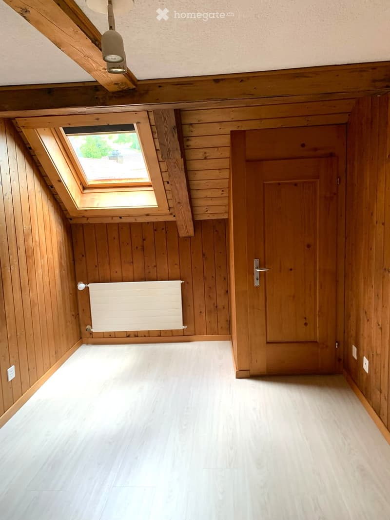 Empty wooden hallway with white tiled floor, skylight window, radiator, and wooden door.