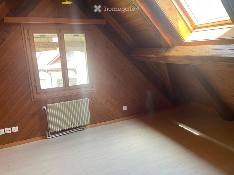 Empty attic room with wooden walls, slanted ceiling, skylight window, radiator, and electrical outlets.