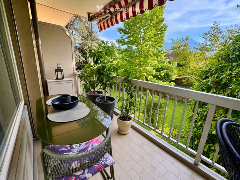 Balcony with a table, chairs, potted plants, and a scenic view of greenery and mountains.