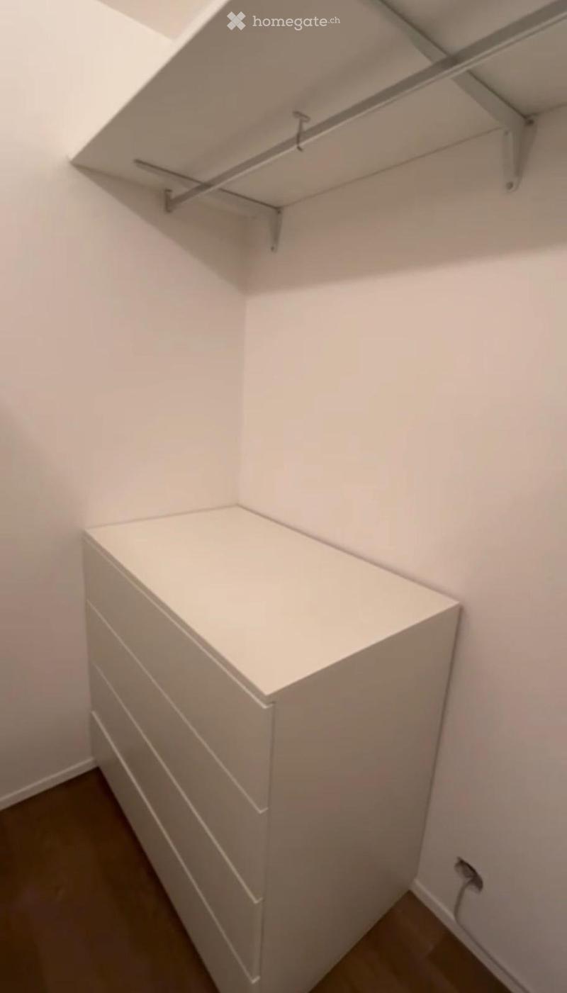 Empty corner of a room with white walls, grey floor, and built-in storage unit with shelves and drawers.