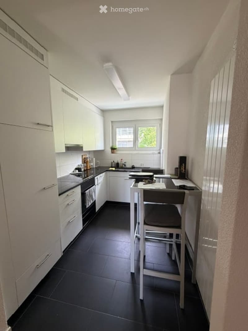 Modern kitchen with white cabinets, black tiled floor, and a small dining area with a table and chair.