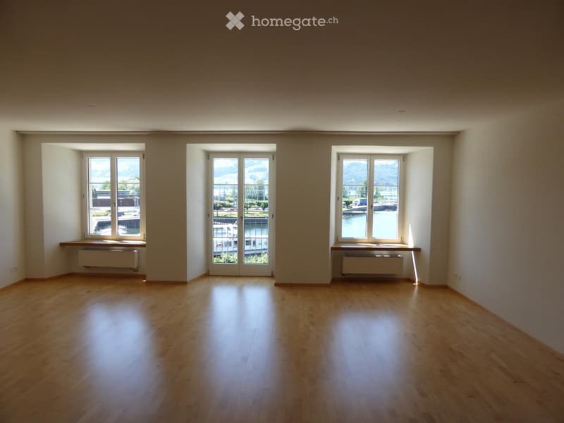 Empty room with wooden flooring, large windows, and sliding glass doors leading to a balcony or outdoor area.