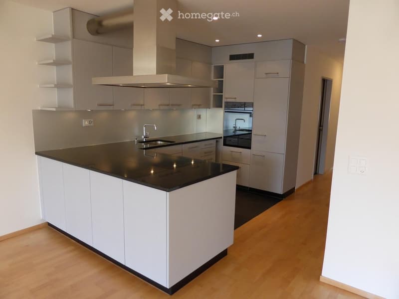 Modern kitchen with white cabinets, black countertops, and a central island. Features a stainless steel sink and faucet, integrated range hood, and built-in appliances.