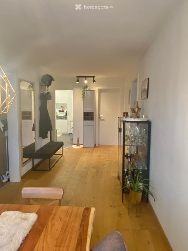 Bright hallway with wooden flooring, modern lighting, and visible adjacent rooms including a kitchen and a dining area.